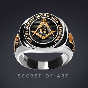 Peut inclure: Une bague en argent avec un incrustation en émail noir représentant un compas et une équerre maçonniques dorés avec la lettre "G" au centre. La bague est gravée des mots "Virtus Junxit Mors Non Separabilit" en lettres dorées.