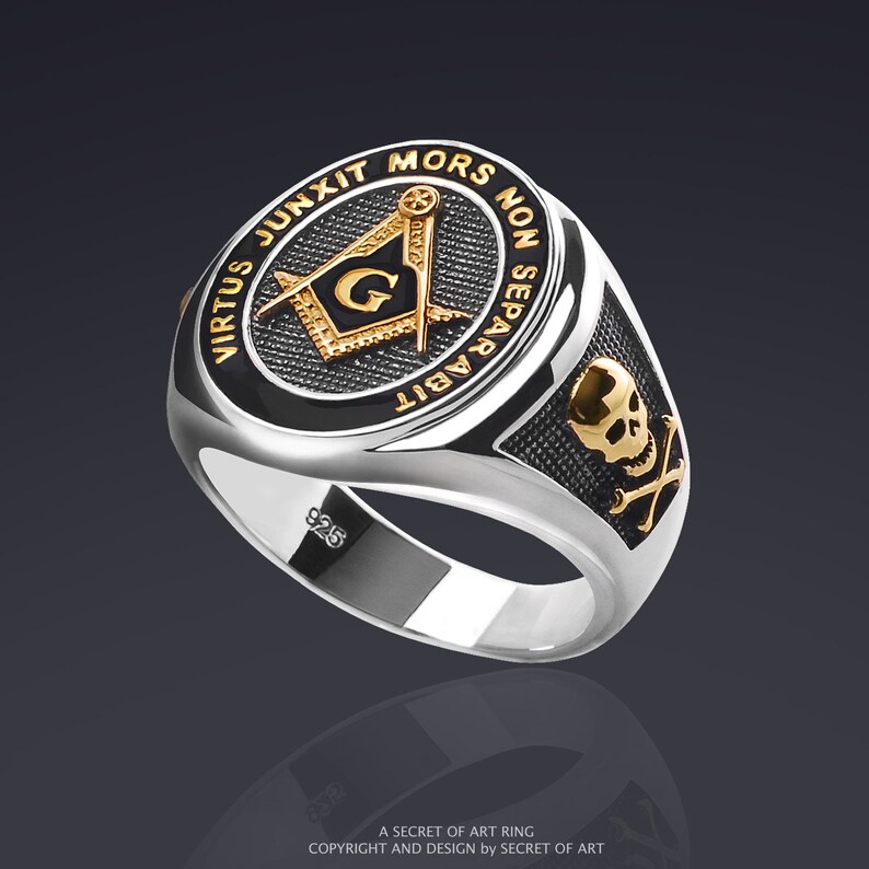 May include: A silver ring with a black enamel center featuring a gold Masonic compass and square with the letter "G" inside. The ring also has a skull and crossbones design on the side. The inscription on the ring reads "Virtus Junxit Mors Non Separabit".