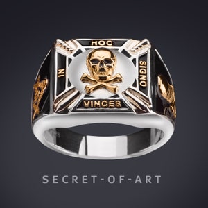 Könnte beinhalten: Ein silberner Ring mit einer schwarzen Emaille-Einlage, die ein goldenes Totenkopf- und Knochenkreuz zeigt. Der Ring trägt die Inschrift "HOC SIGNO VINCES" um den Totenkopf und die Knochen herum.