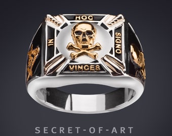 Peut inclure: Une bague en argent avec un incrustation en émail noir représentant un crâne et des os croisés en or. La bague porte l'inscription "HOC SIGNO VINCES" autour du crâne et des os croisés.