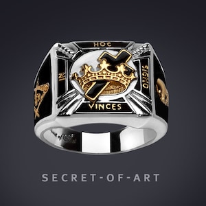 Könnte beinhalten: Ein silberner Ring mit schwarzer Emaille und goldenen Akzenten. Der Ring zeigt ein Kreuz mit einer Krone darüber und die Worte "Hoc In Signo Vinces" darum herum.