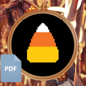 May include: A black and white cross-stitch pattern of a candy corn on a black background. The candy corn is yellow, orange, and white.