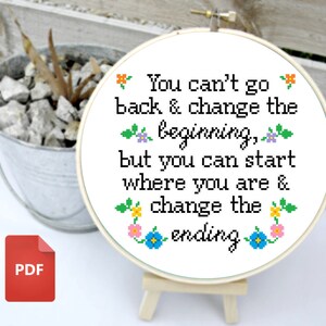 May include: White embroidery hoop with a quote that reads "You can't go back & change the beginning, but you can start where you are & change the ending." The quote is surrounded by colorful flowers.