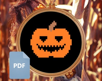May include: A black and orange pixelated pumpkin with a carved face, in a wooden embroidery hoop. The pumpkin is on a brown and yellow background.