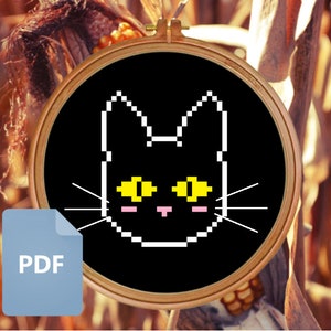 May include: A black and white pixel art cat with yellow eyes in a wooden embroidery hoop. The cat is on a black background. The hoop is in front of a blurry background of corn stalks.