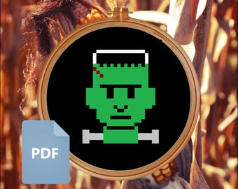 Puede incluir: Una cara de Frankenstein pixelada en negro y verde sobre un fondo negro en un aro de bordado de madera. La imagen es una descarga PDF.