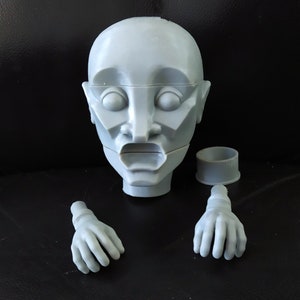 May include: A gray, plastic, articulated puppet head with two hands. The head has a detailed face with a wide open mouth. The hands are separate pieces.