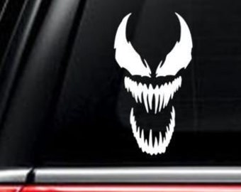 May include: Two Venom character decals, one white and one black, on a car window and door. The decals are of the character's face with a menacing grin and sharp teeth.