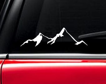 May include: A white mountain range silhouette decal for a car window. The decal is on a black car window.