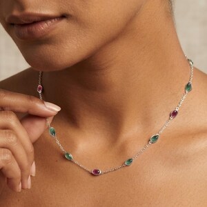 Puede incluir: Un collar de cadena plateada con piedras preciosas en forma de lágrima, engastadas en bisel y espaciadas uniformemente, que alternan tonos rosa intenso y verde bosque. Los delicados eslabones metálicos conectan cada piedra para formar un collar.
