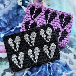 Puede incluir: Dos bolsas de crochet, una morada con formas de fantasmas negros y otra negra con formas de fantasmas blancos.