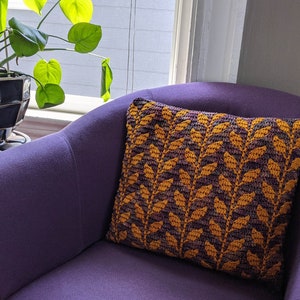 May include: A purple armchair with a crocheted cushion featuring a leafy pattern in shades of brown and gold.