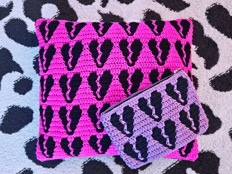Puede incluir: Una almohada de crochet rosa con un patr&oacute;n de coraz&oacute;n negro y una bolsa de crochet morada a juego con un patr&oacute;n de coraz&oacute;n negro.