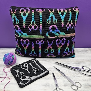 May include: Black crochet pillow with rainbow-colored scissors pattern. A matching coaster and ball of yarn are next to the pillow. Three pairs of scissors are also on the table.