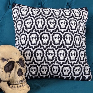 Puede incluir: Una almohada de tiro de color blanco y negro con un patrón de calavera. La almohada está en un sofá turquesa.