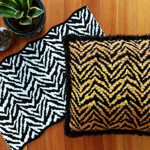 May include: Two crocheted throw pillows with a chevron pattern. One pillow is black and white, and the other is black, gold, and white.