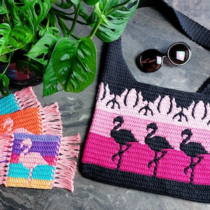 Puede incluir: Una bolsa de mano de crochet negra con rayas rosas y blancas y siluetas de flamencos. La bolsa tiene una correa larga y está decorada con un borde de flecos. También se muestran cuatro posavasos de crochet más pequeños con siluetas de flamencos.