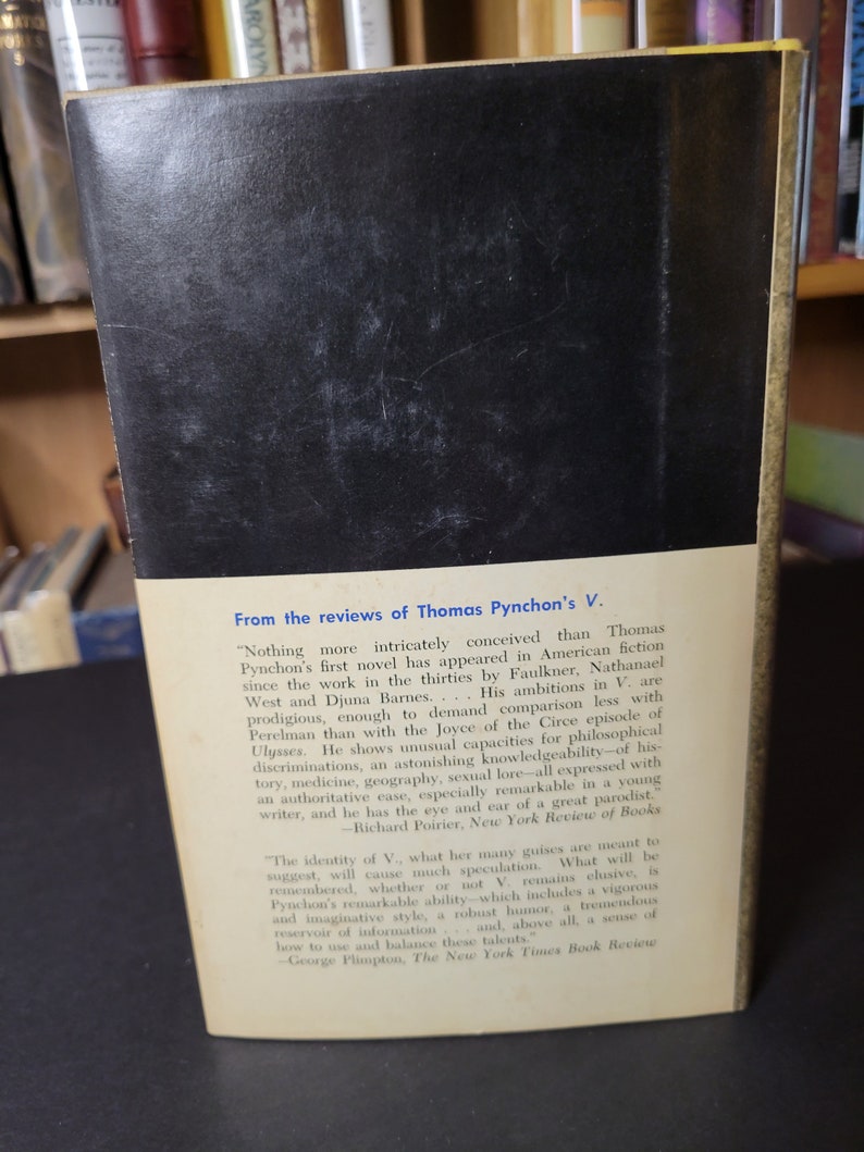 May include: The back cover of a vintage book, featuring a black background and white text. The text includes reviews of Thomas Pynchon's novel "V." from the New York Review of Books and The New York Times Book Review.