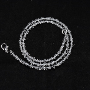 Puede incluir: Un collar de cristal transparente con un cierre plateado. El collar está hecho de pequeños cristales facetados que están enhebrados en una fina cadena plateada.