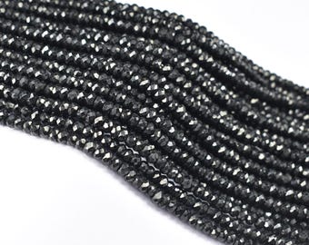 May include: Strands of faceted black beads, likely gemstones, are displayed against a white background. The beads have a sparkling, reflective quality, suggesting they are polished and cut to catch the light. The beads are strung together.