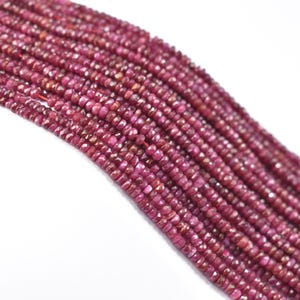 May include: Close-up of multiple strands of faceted ruby beads. The beads are a deep red-pink hue and are strung together. The gemstones are displayed against a white background. Each bead is small and has multiple facets.