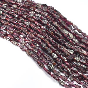 May include: Strands of dark red beads with leaf-like carvings. The beads are strung together, creating a textured and detailed appearance. The beads are a deep burgundy color, with lighter highlights.