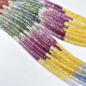 Puede incluir: Primer plano de varios hilos de cuentas de piedras preciosas multicolores. Las cuentas son pequeñas, facetadas y de colores amarillo, morado, azul y verde. Están ensartadas, ideales para la creación de joyas.
