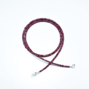 May include: A delicate necklace made of small, faceted ruby beads. The necklace is strung on a silver chain and has a lobster clasp closure.