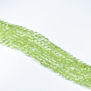 May include: Strands of light green peridot gemstone beads. The beads are oval-shaped and have a faceted surface, creating a sparkling effect. The beads are strung together, ready for jewelry making.