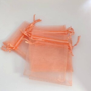 May include: A stack of peach-colored organza gift bags with drawstrings. The bags are made of sheer fabric and are perfect for small gifts or favors.