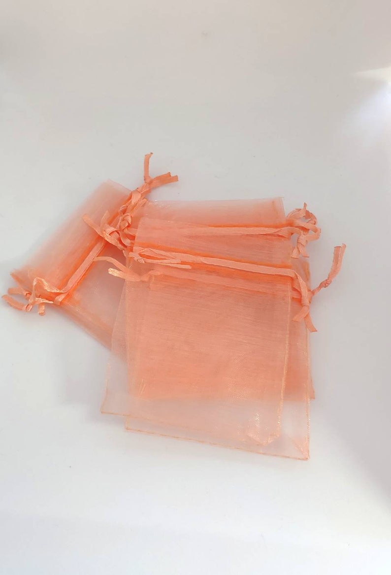 May include: A stack of peach-colored organza gift bags with drawstrings. The bags are made of sheer fabric and are perfect for small gifts or favors.