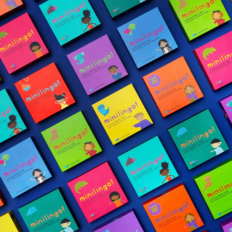 Pu&ograve; includere: Una collezione di scatole quadrate per il gioco di memoria bilingue Minilingo! in vari colori, tra cui rosa, arancione, giallo, verde, verde acqua e viola. Ogni scatola presenta il testo Minilingo!, un animale e un bambino illustrati.