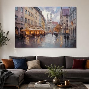 Peut inclure: Une impression d'art mural rectangulaire représentant une scène de rue urbaine européenne avec des immeubles à plusieurs étages, une grande église aux flèches jumelles au loin, une terrasse de café éclairée et des piétons sur une rue humide.