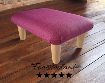 May include: A pink fabric footstool with wooden legs. The footstool is on a wooden floor. The text "Footstooland" and five stars are visible below the footstool.