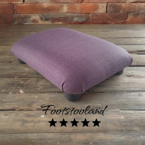 May include: A rectangular footstool with a purple fabric top and four dark gray legs. The footstool is on a wooden surface. The text "Footstooland" and five black stars are visible.
