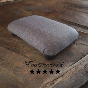 May include: A gray fabric footstool with black legs. The footstool is on a wooden surface. Footstool and is rated five stars.