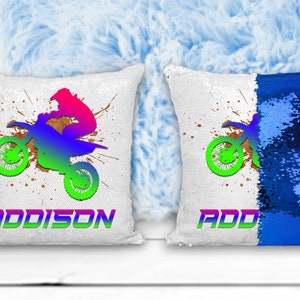 Puede incluir: Dos almohadas de lentejuelas blancas y azules con un gráfico de un piloto de motocross y el nombre "ADDISON" en una almohada. Las almohadas son reversibles y el otro lado es azul sólido.