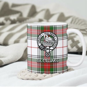 May include: White ceramic mug with a green, red and white tartan pattern. The mug features a crest with a bird and the text "VIRECIT VULNERE VIRTUS" and "STEWART".