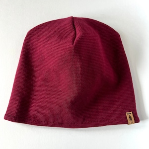 May include: A burgundy waffle knit beanie with a small brown leather patch featuring a tree logo.