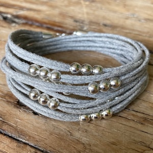 Può includere: Un braccialetto grigio a più fili con perline d'argento. Il braccialetto è realizzato in un materiale morbido e intrecciato e ha un design semplice ed elegante.