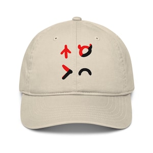Può includere: Un cappellino da baseball beige con un design grafico sul pannello frontale. Il design è composto da quattro simboli distinti disposti in una griglia quadrata, realizzati in colori rosso e nero, tra cui una freccia, una forma di corno e curve.