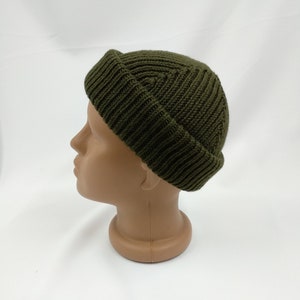 May include: A dark green knitted beanie with a ribbed texture. The beanie is folded down at the top, creating a unique shape.