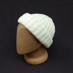 May include: A white knitted beanie with a ribbed texture. The beanie is folded down at the brim.