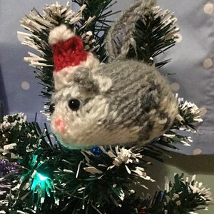 May include: A gray and white knitted hamster wearing a red Santa hat, hanging on a Christmas tree.