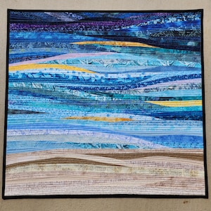 May include: Abstract wall art quilt with a layered design of blue, yellow, and purple fabric strips. The quilt is quilted in a wavy pattern, creating a sense of movement and depth. The quilt is framed with a black border.