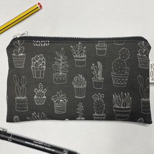 May include: A black zippered pouch with a white cactus and succulent print. The pouch has a white label with the text "Red One Design".
