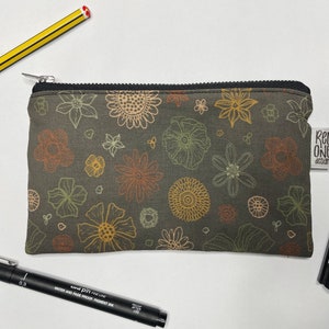 May include: A small zippered pouch with a floral print in shades of brown, yellow, and orange. The pouch has a black zipper and a small label that says "Red One Design".