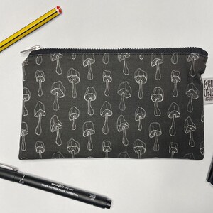 May include: A black zippered pouch with a white mushroom pattern. The pouch has a white label with the text "Red One Design".
