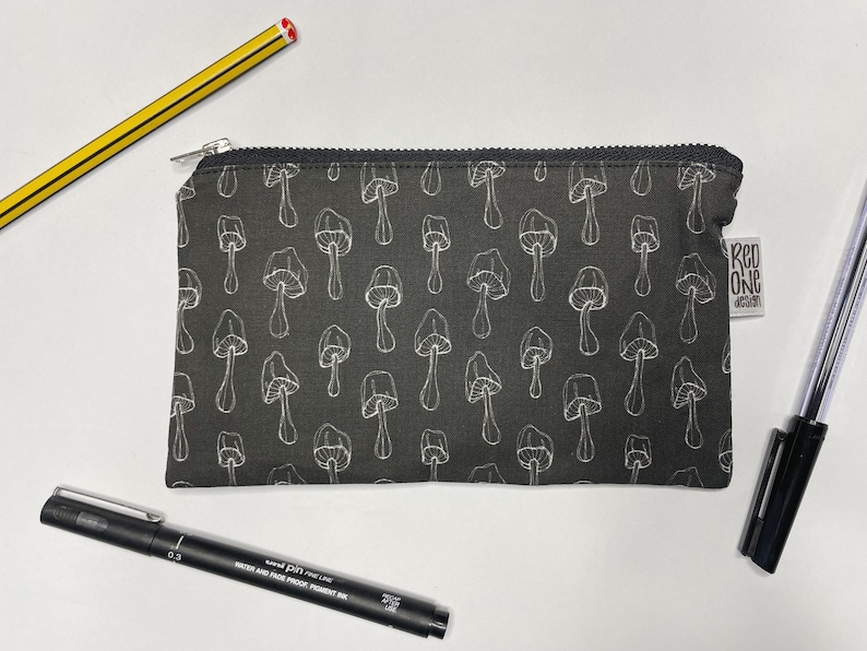 May include: A black zippered pouch with a white mushroom pattern. The pouch has a white label with the text "Red One Design".