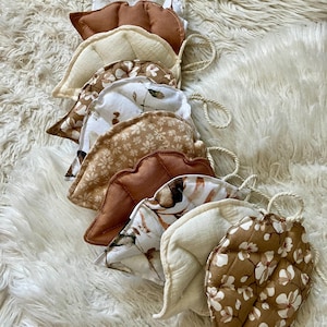 Può includere: Una ghirlanda di ornamenti in tessuto a forma di foglia in varie tonalità di marrone, crema e bianco, con motivi floreali e trapuntati. Ogni foglia è attaccata a uno spago naturale, adatta per essere appesa o decorare.